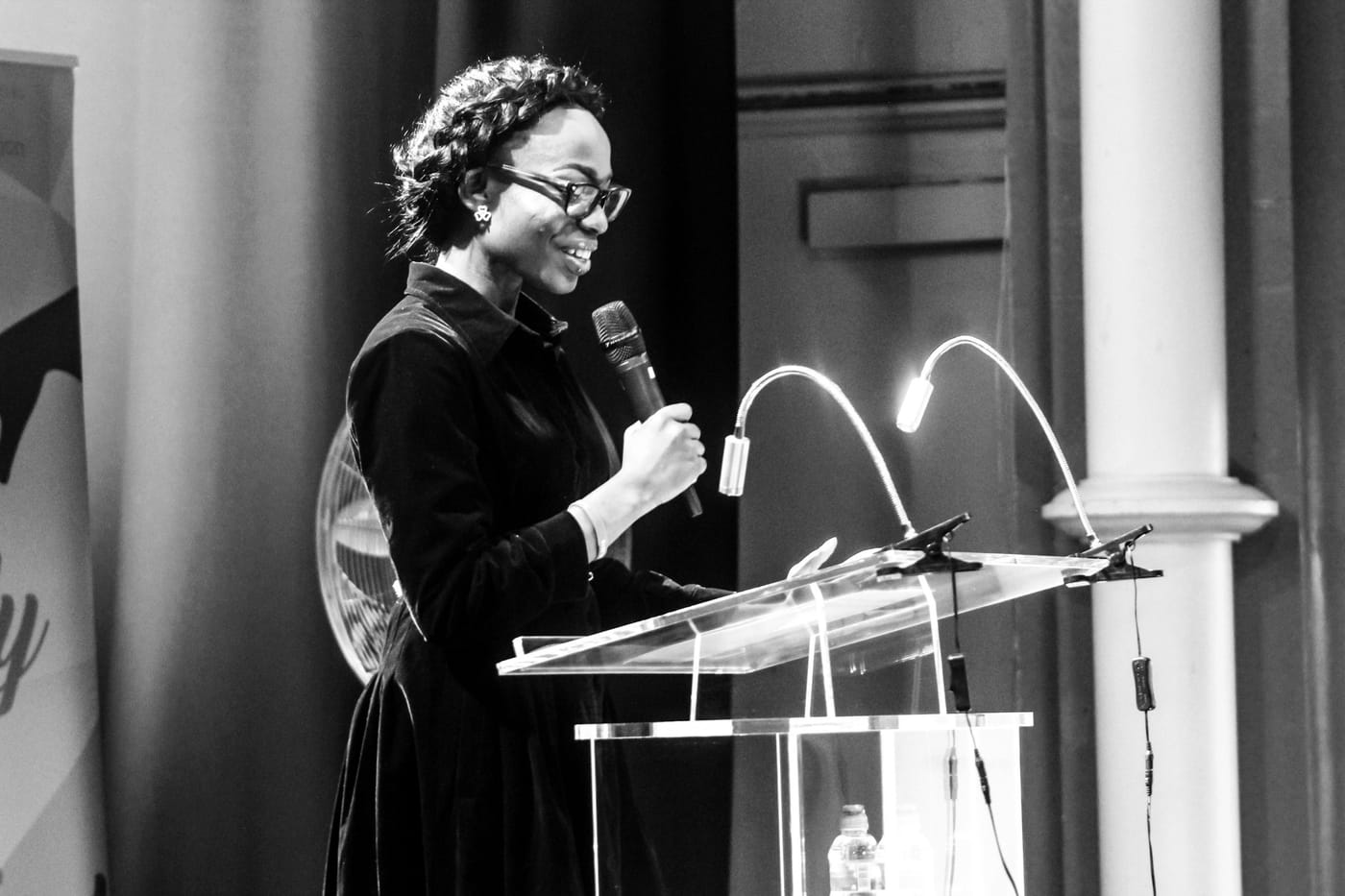 DK Jonah smiling as she speaks into a microphone at a lectern